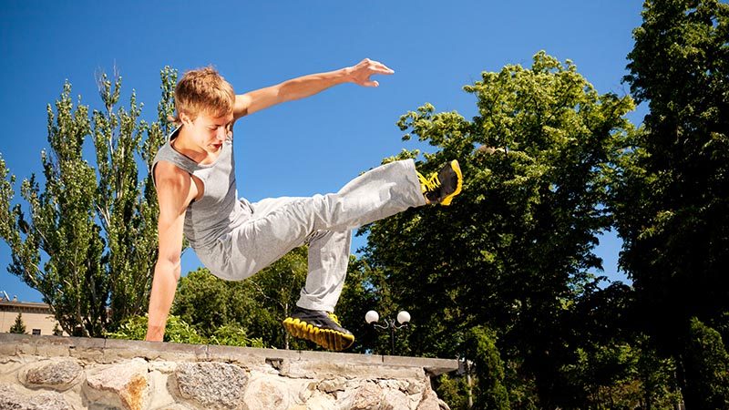 Young man in sportswear practicing parkour outside on stone wall on clear summer day with blue sky at background. Active lifestyle and extreme sports concept