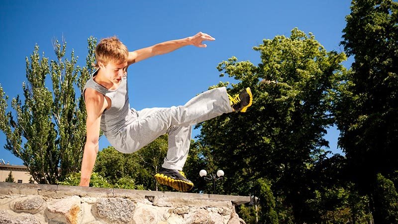 Young man in sportswear practicing parkour outside on stone wall on clear summer day Young man in sportswear practicing parkour outside on stone wall on clear summer day with blue sky at background. Active lifestyle and extreme sports concept